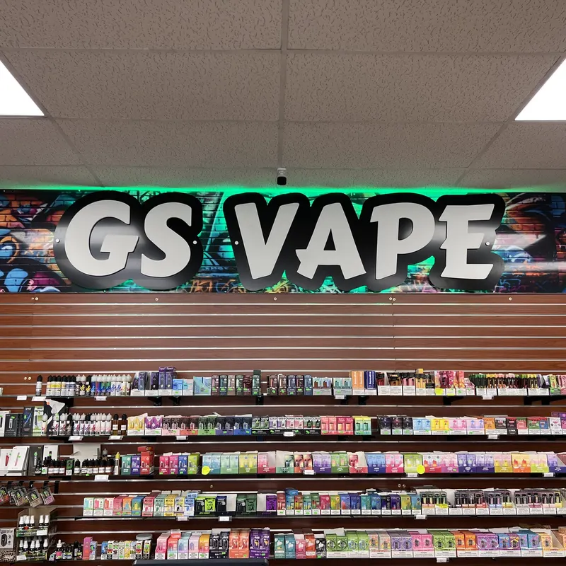 The backlit GS Vape logo sign inside the Barberton, Ohio location, mounted above the vape and accessory wall. Illuminated GS Vape logo sign above product shelves inside the Barberton, Ohio store